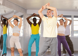 Enthusiastic young man energetically participating group choreography class with men and women of...