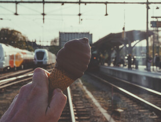 Cropped hand holding a ice cream against a train station