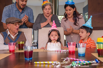 Hispanic family: parents, grandparents and grandchildren get together to celebrate a girl's birthday.
The girl blows out her candle and makes a wish.