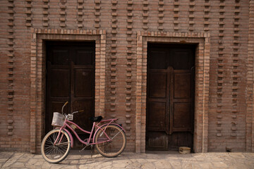 Fototapeta na wymiar bicicleta retro color rosa enfrente de casa vieja de pueblo de viesca, coahuila 