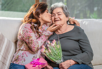 Daughter kisses her mother on the cheek and gives her a beautiful bouquet of flowers