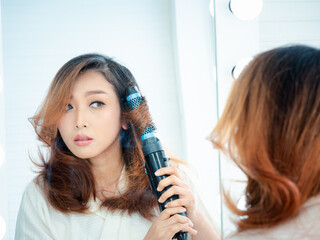 Fototapeta premium Portrait of a beautiful Asian woman doing her makeup in front of a mirror. Beautiful Asian woman applying lipstick near the cosmetic table..