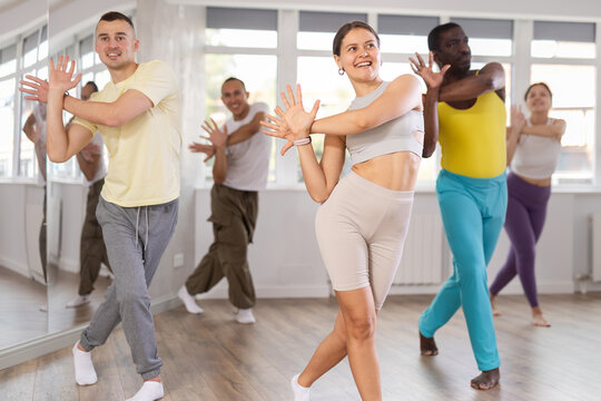 Smiling sporty active young girl enjoying contemporary vigorous dance at group class with men and women of different ages and nationalities in light mirrored studio