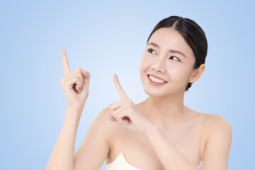 Close-up portrait of young Asian beautiful woman with healthy skin pointing finger isolated on light blue background for skincare commercial product advertising.