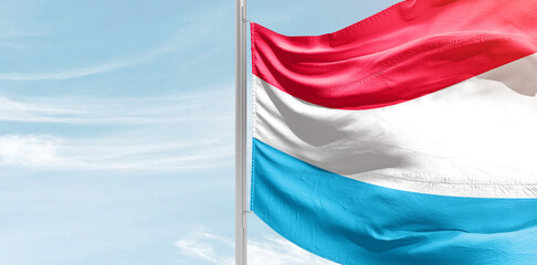 Luxembourg national flag with mast at light blue sky.