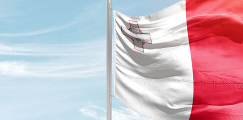 Malta national flag with mast at light blue sky.