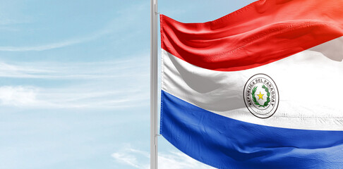 Paraguay national flag with mast at light blue sky.
