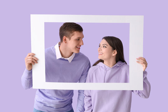 Happy young couple with frame on lilac background
