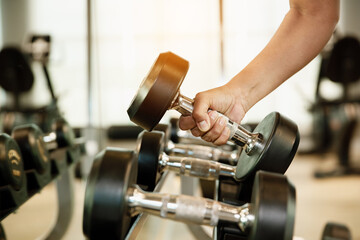 Close up hand holding dumbbell on floor in gym with woman background. Object goal weightlifting...