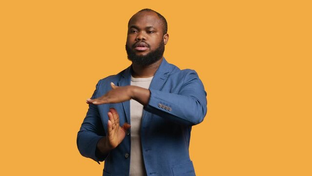 Portrait of assertive BIPOC man asking for timeout, doing hand gestures, feeling fatigued. Unhappy person doing vehement pause sign gesturing, wishing for break, studio background, camera A