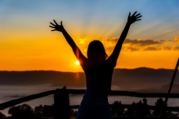 Silhouette happy woman on the sunrise in nature in winter with raising hands