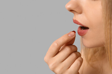 Young woman taking vitamin A pill on light background, closeup