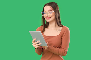 Fototapeta premium Young woman in eyeglasses using tablet computer on green background