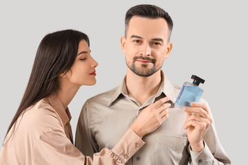 Young couple with perfume on light background