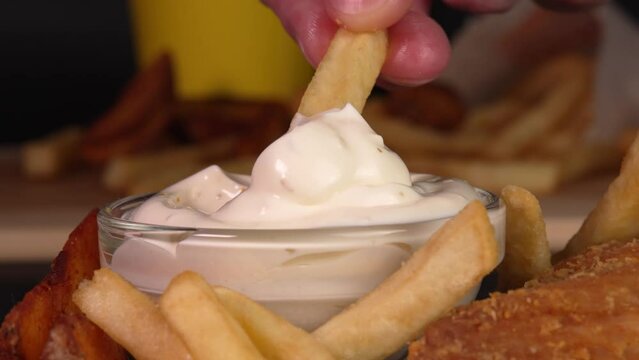 Hand dips crunchy french fries into garlic sause in macro. Footage for advertise fast food, takeaway junk food, roadside cafe, supermarket display, food truck, street food