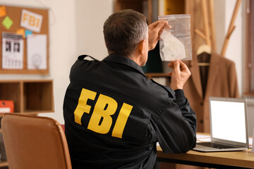 Mature FBI agent with evidence at table in office, back view