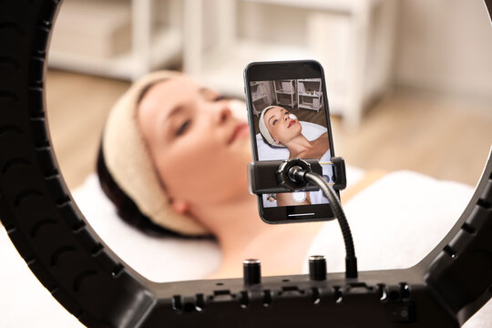 Beautiful woman with facial mask on screen of mobile phone in beauty salon, closeup