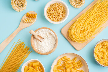 Bowls with different uncooked pasta on blue background
