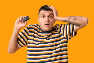 Shocked young man with car key on yellow background