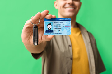 Young happy man showing driver license and car keys on green background