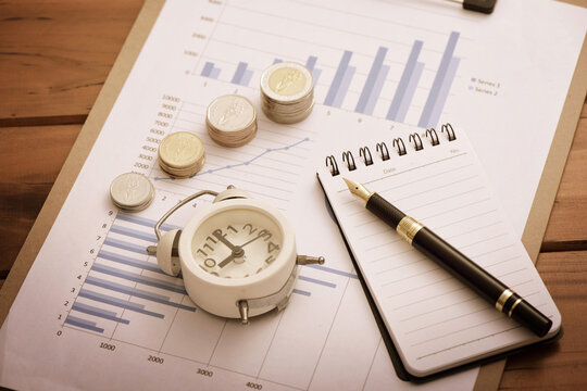 Coins, alarms, and pens placed on financial data reports