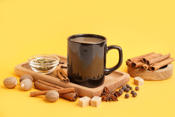 Cup of tasty masala tea with different spices on yellow background