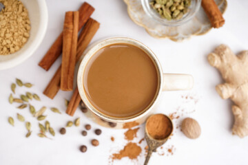 Cup of tasty masala tea with different spices on light background