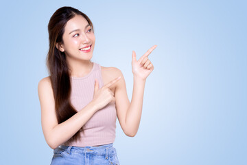Asian Smiling woman pointing finger to the side isolated on blue background with copy space.