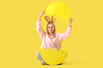 Young girl with Easter bunny ears and big broken paper egg on yellow background
