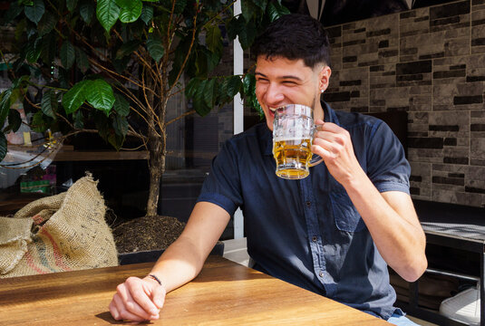 A man is sitting at a table cita a mug of beer in his hand