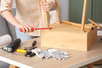 Beautiful young woman with screwdriver assembling wooden table at home, closeup