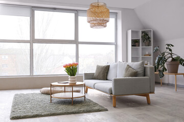 Stylish interior of light living room with large window and cozy sofa