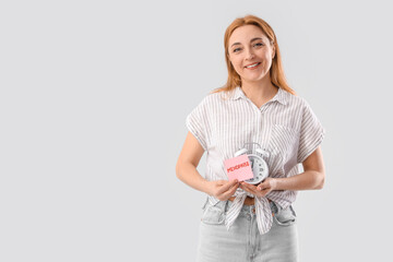Mature woman holding paper with word MENOPAUSE and alarm clock on light background