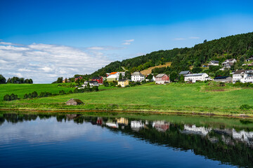 Fototapeta na wymiar Tranquil summer day in norwegian village overlooking the fjord. Kvanne village against forested hillside on a sunny day, with serene reflective waters of the Stangvikfjord in Møre og Romsdal, norway