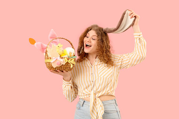 Beautiful young shocked woman in bunny ears with Easter basket on pink background