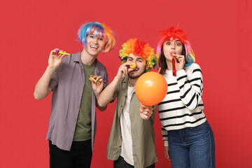 Young friends in funny disguise with party whistle and balloon on red background. April fool's day celebration