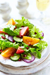 Salad with red and yellow Tomatoes and Pomegranate Seeds on bright wooden Background. Close up.	