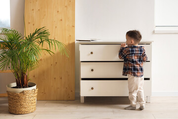 Little boy opening drawers at home, back view. Child in danger