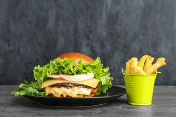 Plate with tasty burger and french fries on grey grunge background