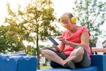 Senior woman listening to music sitting on a blue bench in the park outdoors. lifestyle concept