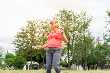 happy retired woman dancing while listening to music with her smartphone outdoors