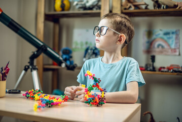 A child boy in the children's room is playing with a toy constructor for teaching the science of chemistry. Assembling molecules from elements. Children's scientific education - 785856534
