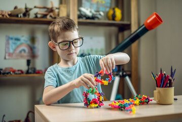 A child boy in the children's room is playing with a toy constructor for teaching the science of chemistry. Assembling molecules from elements. Children's scientific education - 785856982