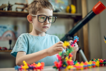 A child boy in the children's room is playing with a toy constructor for teaching the science of chemistry. Assembling molecules from elements. Children's scientific education - 785857344