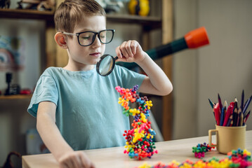 A child boy in the children's room is playing with a toy constructor for teaching the science of chemistry. Assembling molecules from elements. Children's scientific education - 785857963