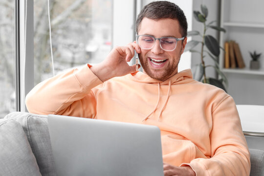 Portrait of male programmer with laptop talking by phone on sofa in office