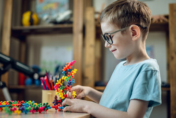 A child boy in the children's room is playing with a toy constructor for teaching the science of chemistry. Assembling molecules from elements. Children's scientific education - 785858587