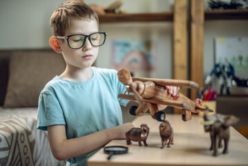 A child boy in the children's room is playing with a toy wooden airplane with animals of the savannah. Fantasies of great adventures and travels - 785858738