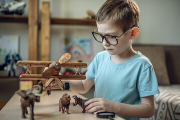 A child boy in the children's room is playing with a toy wooden airplane with animals of the savannah. Fantasies of great adventures and travels - 785858937