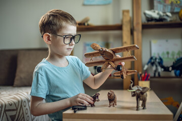 A child boy in the children's room is playing with a toy wooden airplane with animals of the savannah. Fantasies of great adventures and travels - 785859383